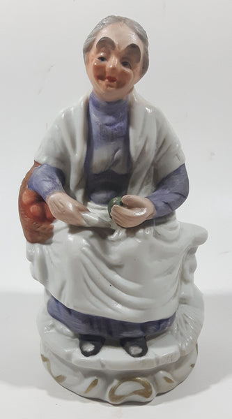 Old Woman Sitting with Basket of Bread Holding a Pear and Banana 6 1/2" Tall Porcelain Figurine